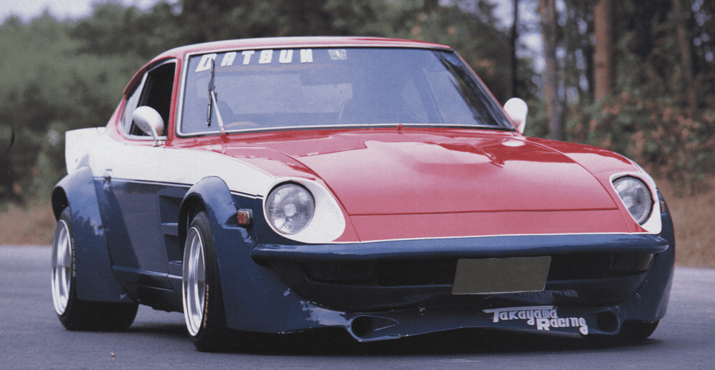Custom red and blue vintage sports car with wide body kit on a road, showcasing unique design elements.